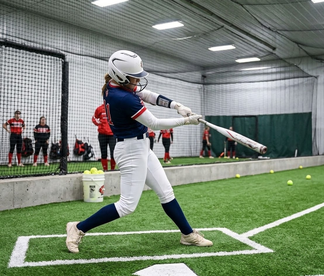 Softball athlete swinging the bat in an indoor training facility